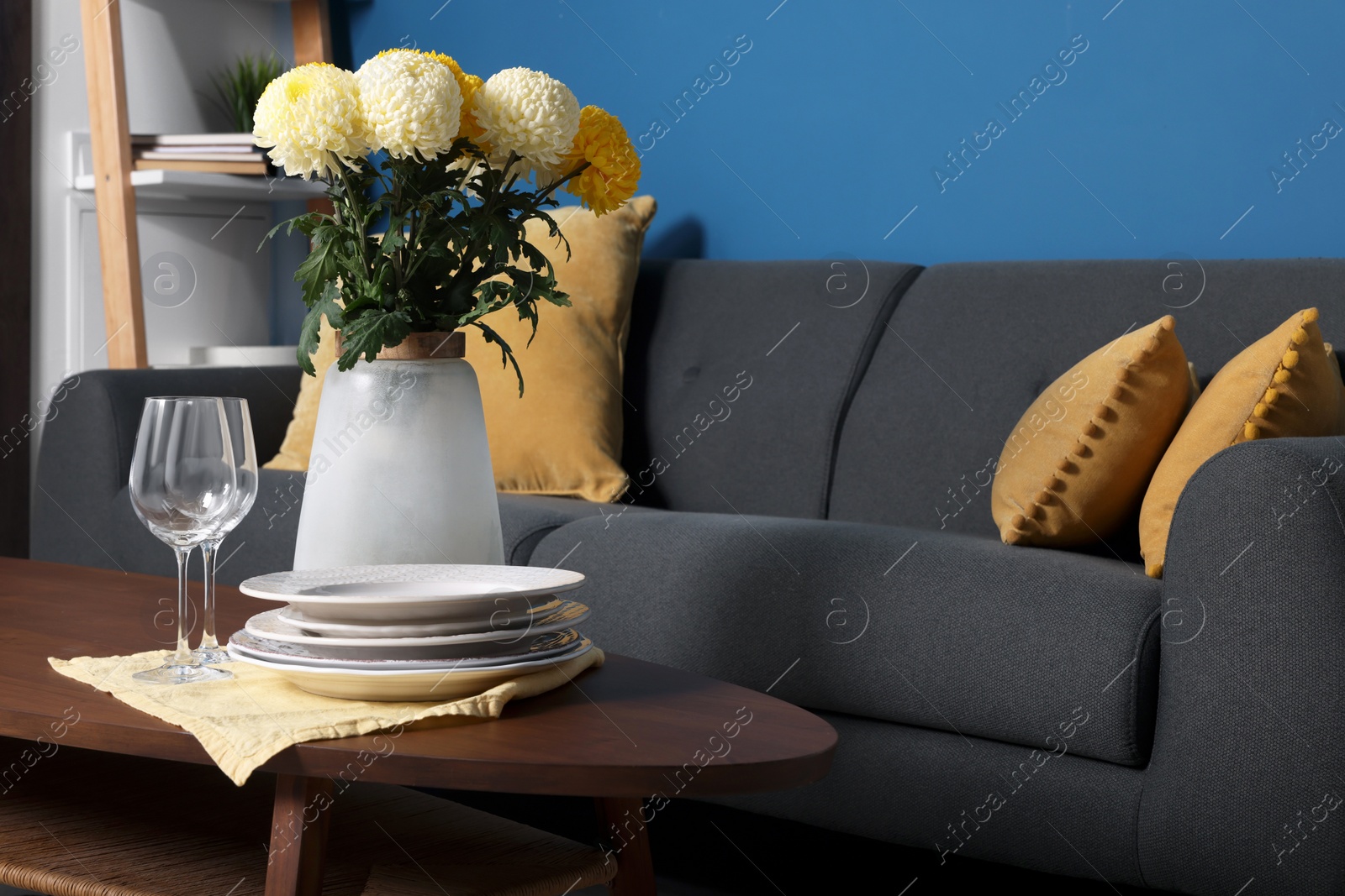 Photo of Vase with beautiful flowers, glasses and plates on wooden table in living room. Interior element