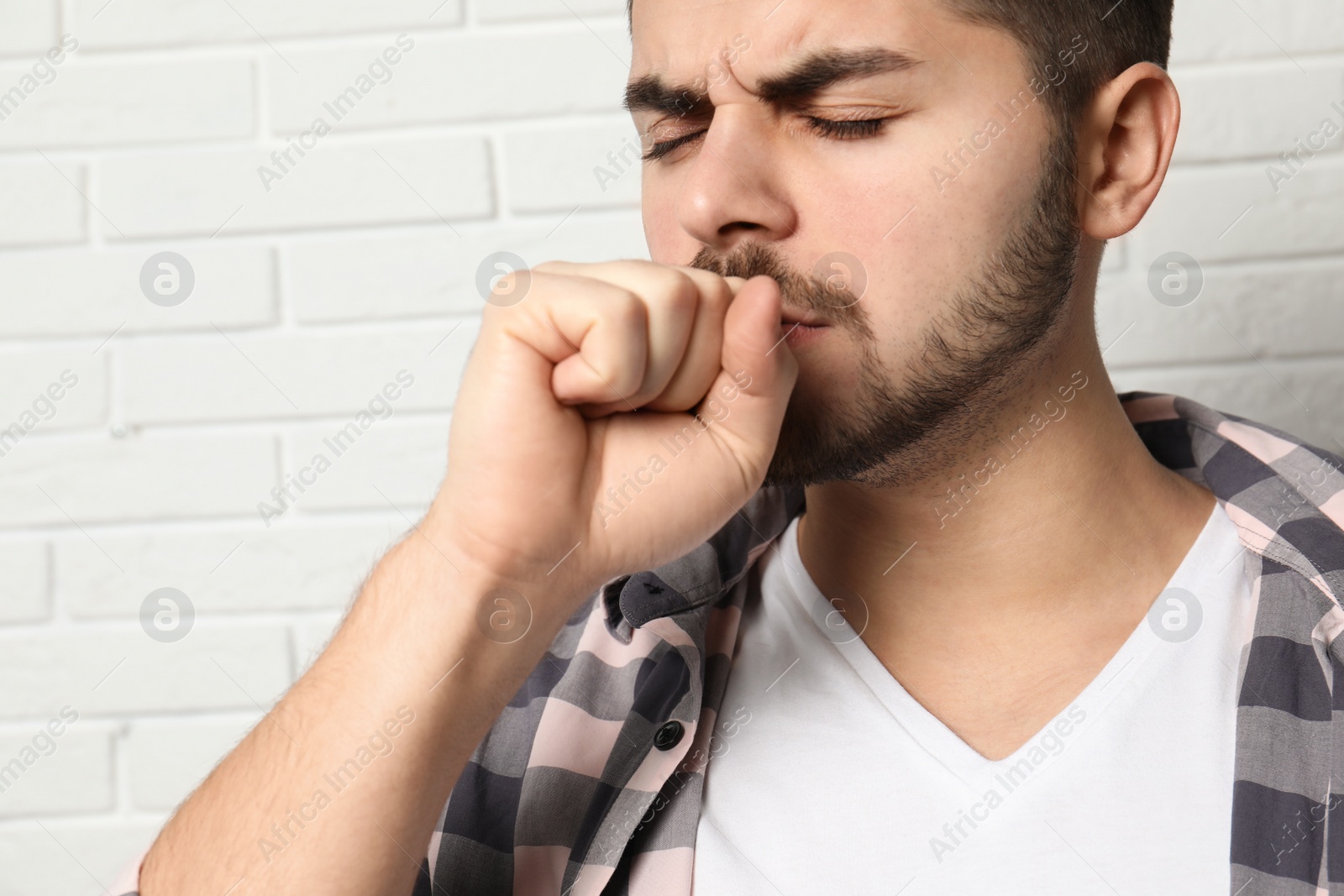 Photo of Handsome young man coughing near brick wall
