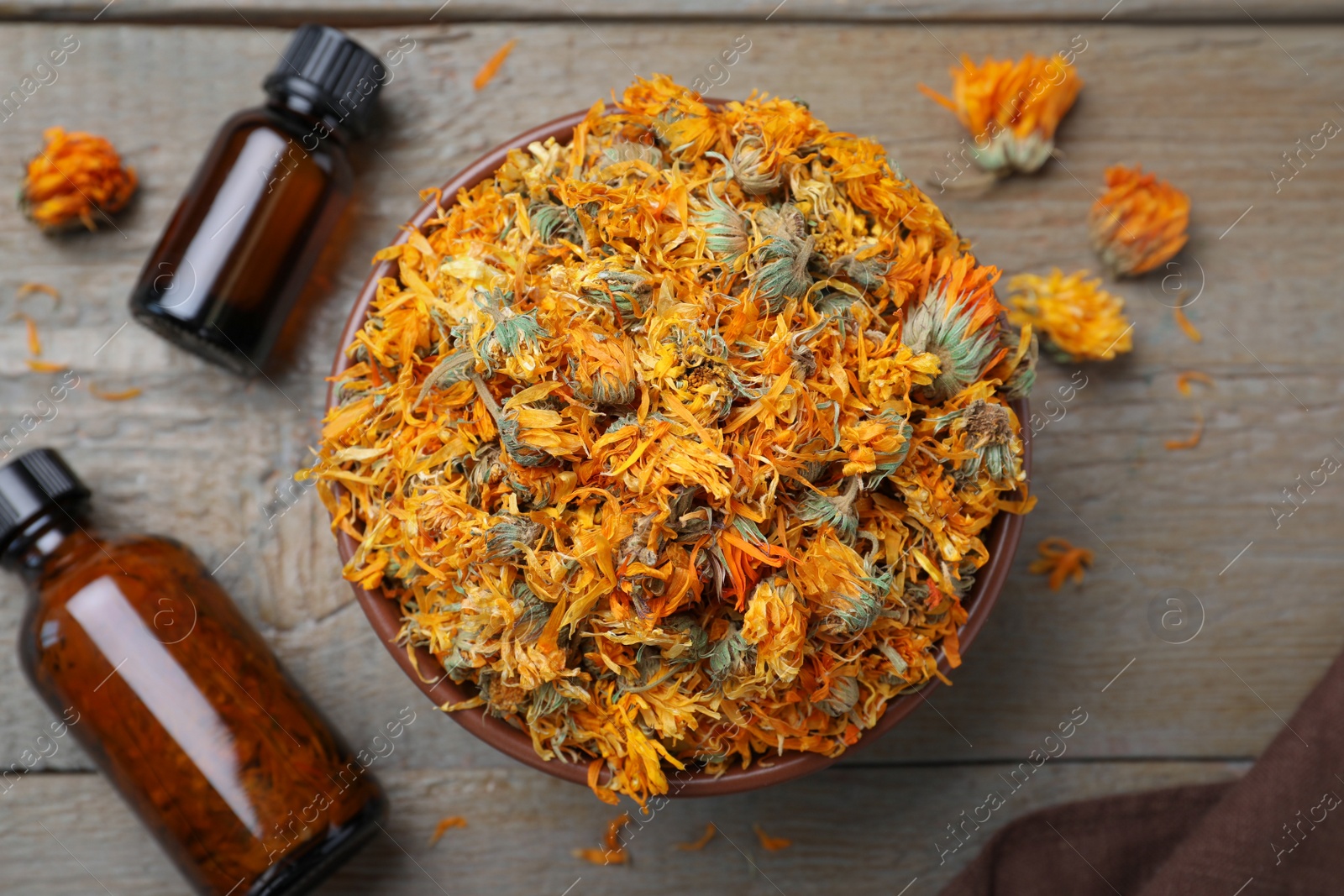 Photo of Dry calendula flowers and bottles with tincture on wooden table, flat lay