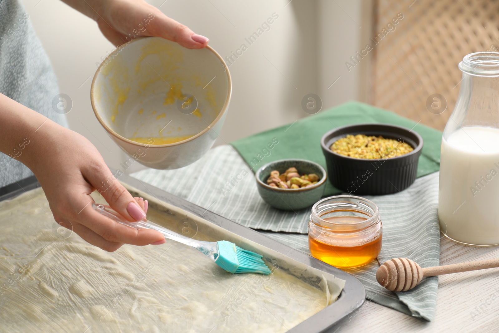 Photo of Making delicious baklava. Woman buttering dough in baking pan at white wooden table, closeup