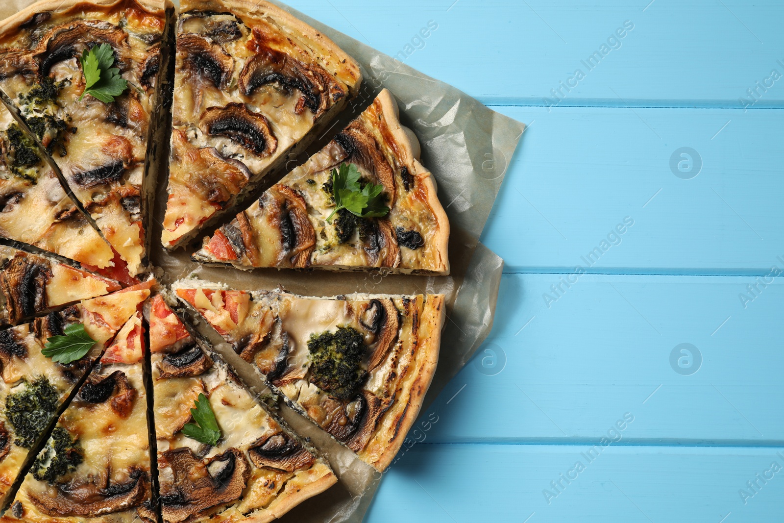 Photo of Delicious quiche with mushrooms and parsley on light blue wooden table, top view. Space for text