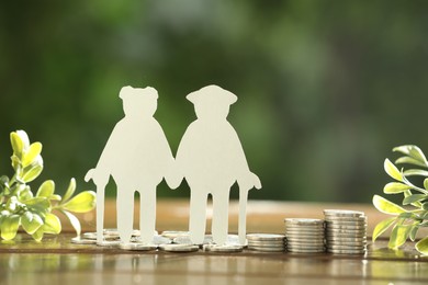 Photo of Pension savings. Figure of senior couple, coins and green twigs on wooden table outdoors