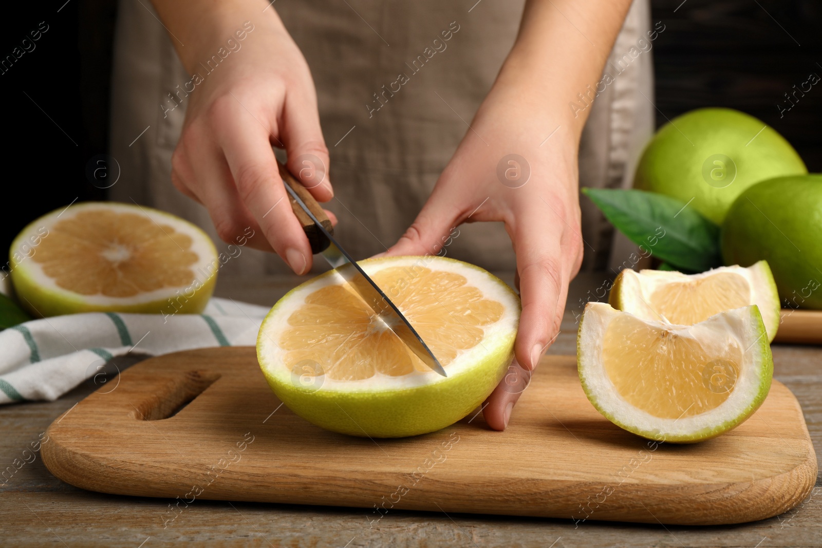 Photo of Woman cutting fresh ripe sweetie fruit at wooden table, closeup
