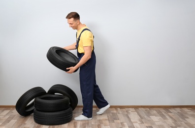 Male mechanic with car tires on light wall background