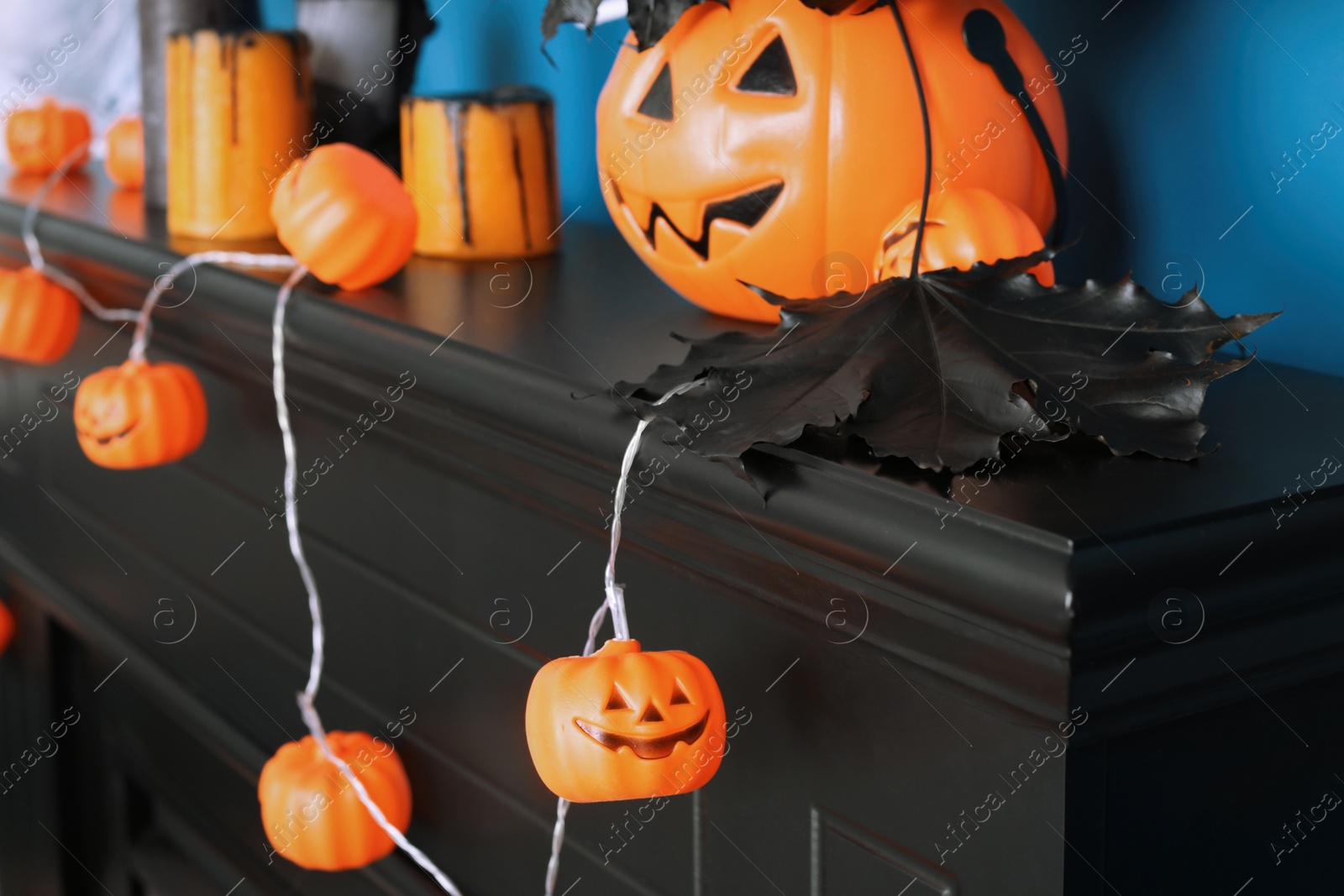 Photo of Jack-o'-lantern lights and black maple leaves on wooden fireplace near blue wall