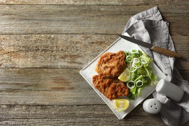 Tasty schnitzels served with lemon and salad on wooden table, flat lay. Space for text