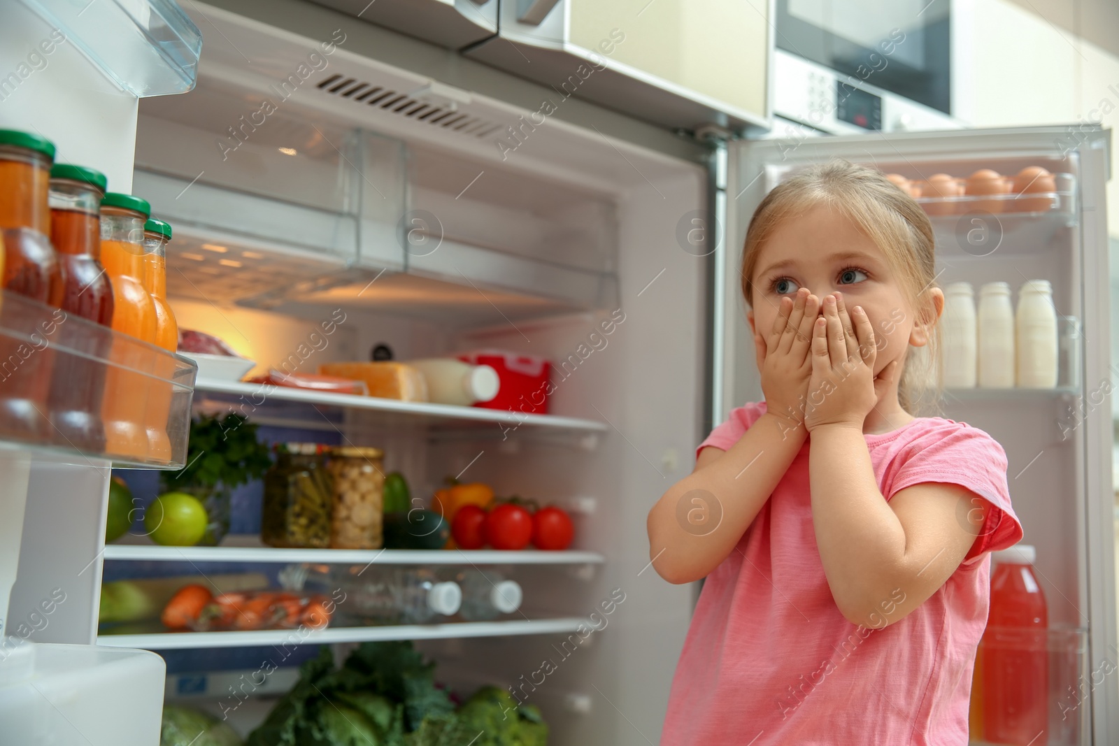Photo of Little girl near bad smelling refrigerator at home