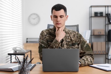 Photo of Military service. Young soldier working with laptop at table in office