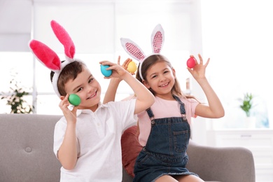 Photo of Cute little children in bunny ears headbands playing with Easter eggs at home