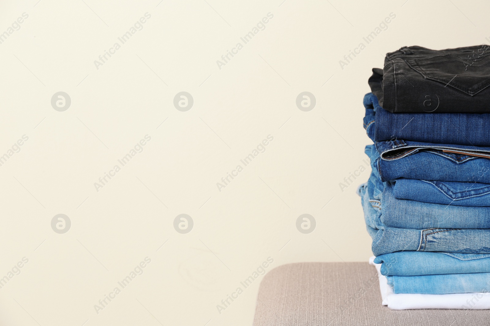 Photo of Stack of different jeans on ottoman against light background. Space for text