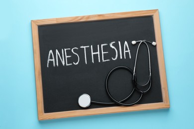 Photo of Blackboard with word Anesthesia and stethoscope on light blue background, top view