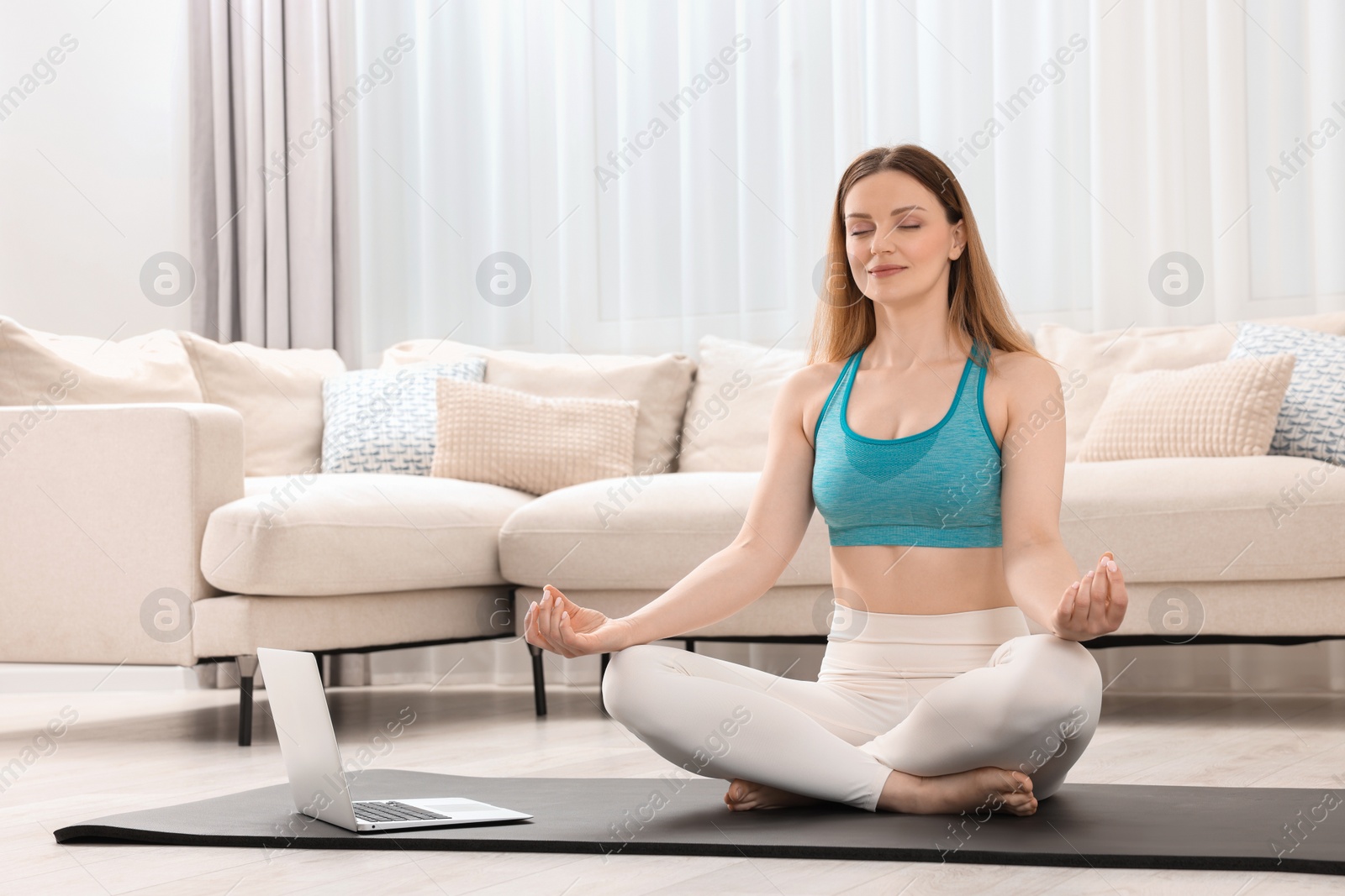 Photo of Woman in sportswear meditating near laptop at home. Harmony and zen