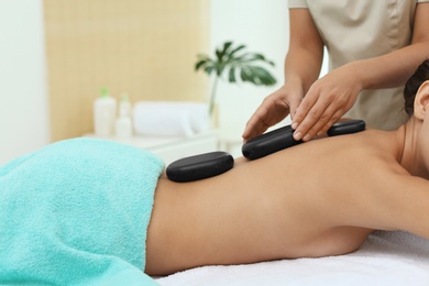 Photo of Beautiful young woman getting hot stone massage in spa salon