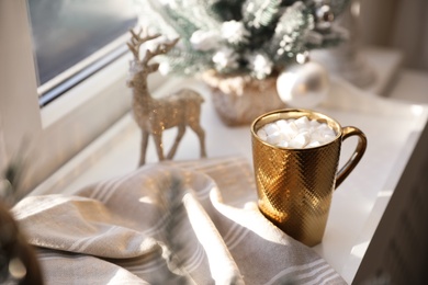 Photo of Golden cup of cocoa and Christmas decor on window sill indoors