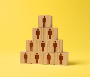 Image of Team and management concept. Pyramid of wooden cubes with human icons on yellow background