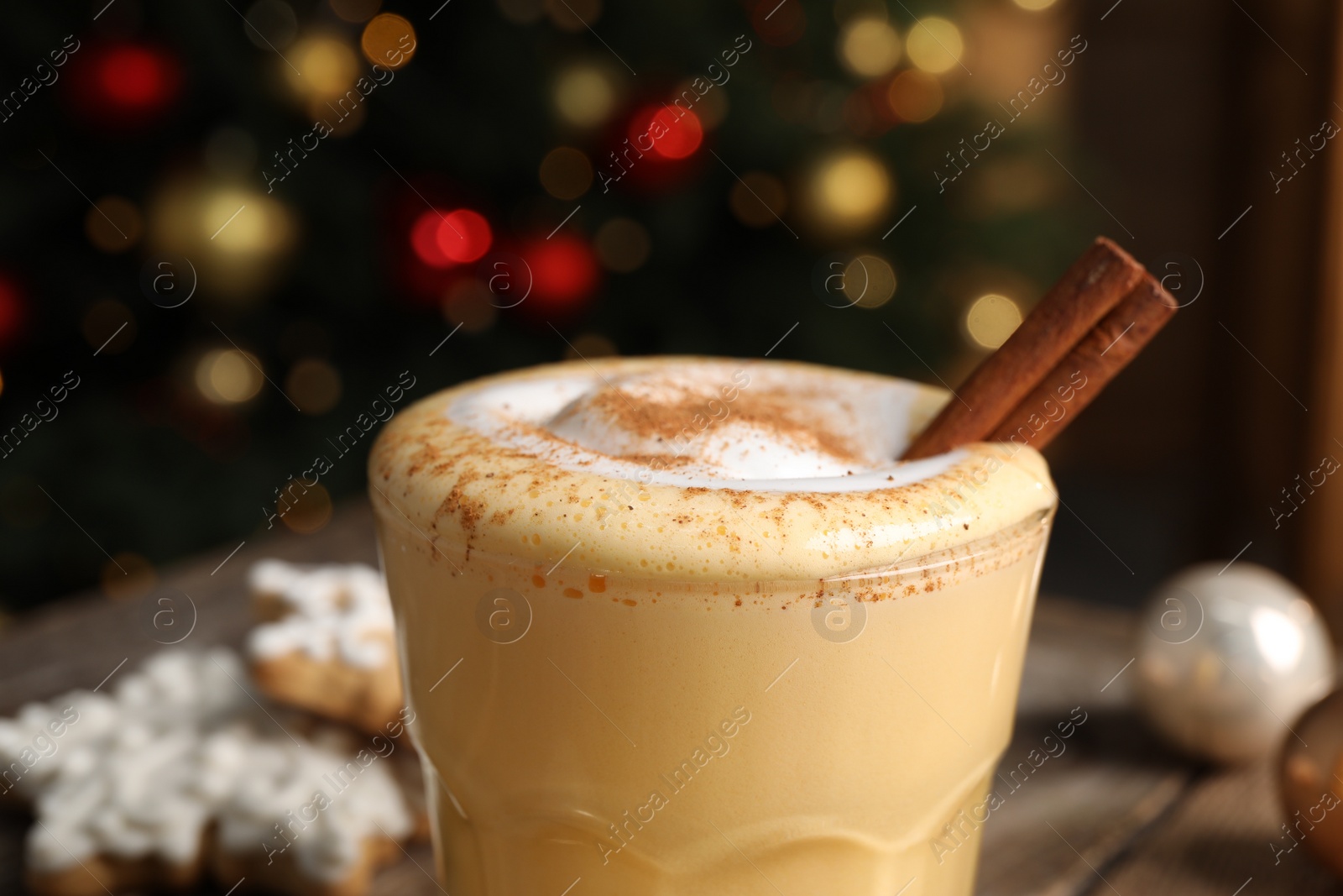 Photo of Tasty eggnog with cinnamon against blurred festive lights, closeup