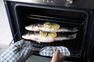 Woman putting rack with sea bass fish, lemon and thyme into oven, closeup