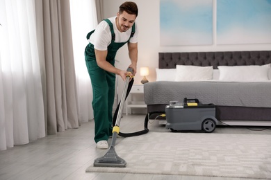 Photo of Professional janitor removing dirt from carpet with vacuum cleaner in bedroom