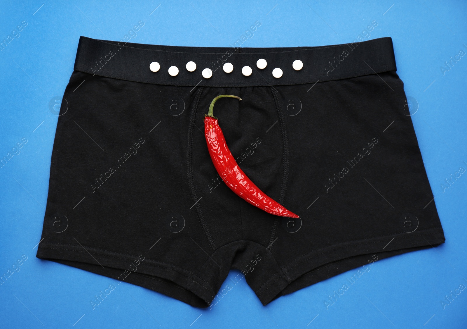 Photo of Men's underwear with chili pepper and pills on blue background, top view. Potency problem concept