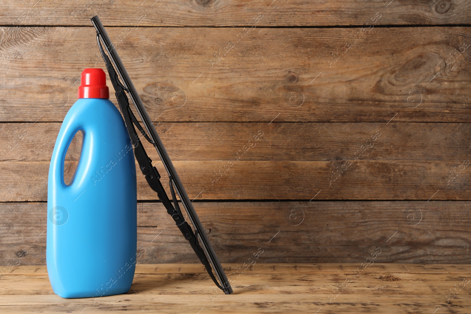 Photo of Bottle of windshield washer fluid and wiper on wooden table. Space for text