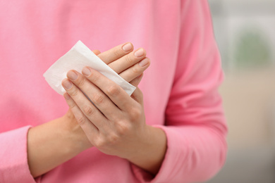 Photo of Woman cleaning hands with paper tissue on blurred background, closeup