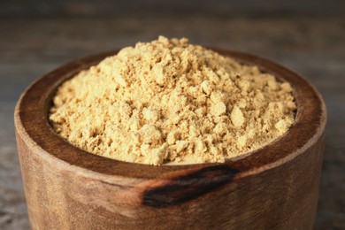 Photo of Bowl of mustard powder on wooden table, closeup