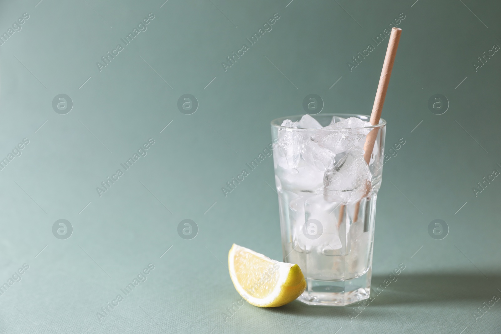 Photo of Refreshing drink with ice cubes in glass and lemon slice on light green background, closeup. Space for text