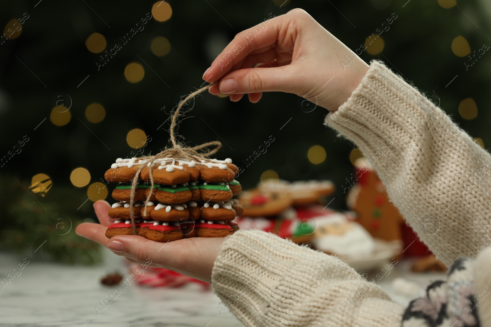 Photo of Woman with decorated cookies against blurred Christmas lights, closeup