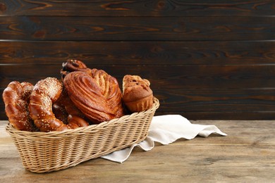 Photo of Wicker basket with different tasty freshly baked pastries on wooden table, space for text