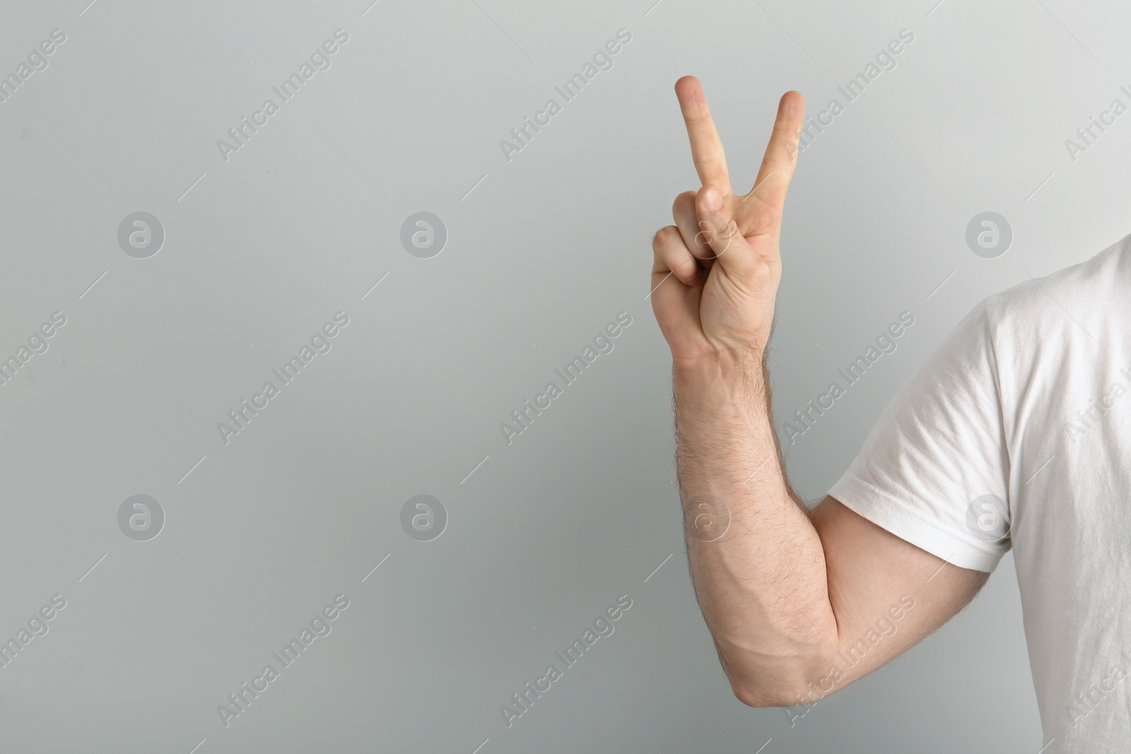 Photo of Young man showing victory gesture on light background. Space for text