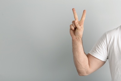 Photo of Young man showing victory gesture on light background. Space for text