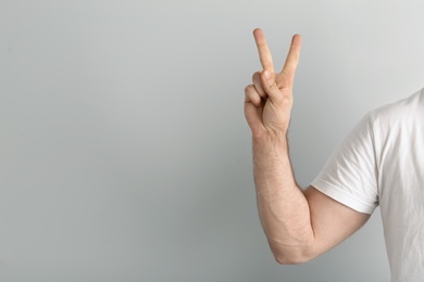 Young man showing victory gesture on light background. Space for text