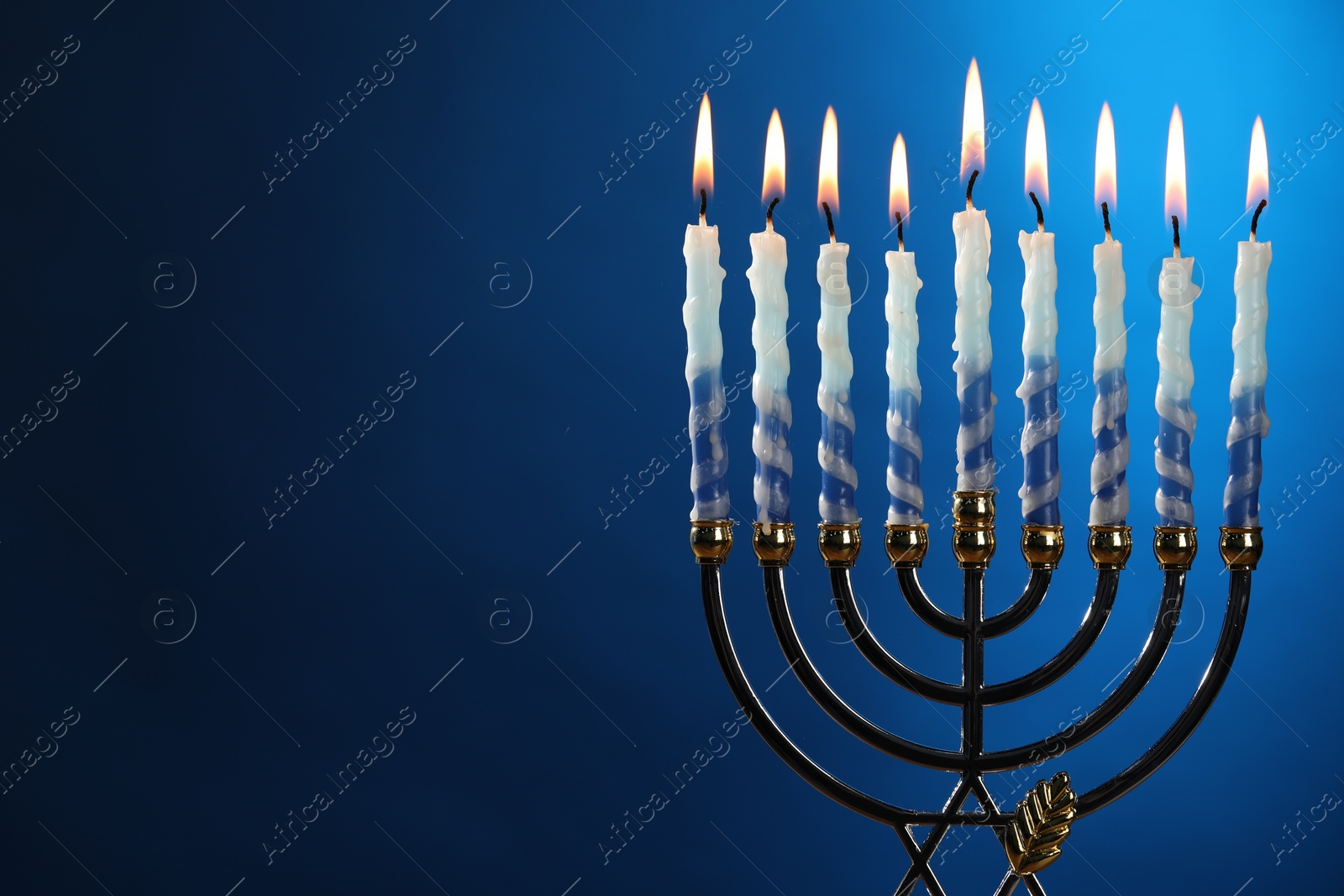 Photo of Hanukkah celebration. Menorah with burning candles on blue background, space for text