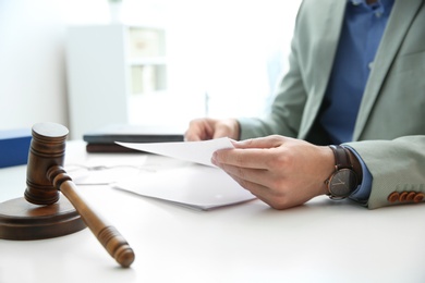 Photo of Notary working with papers and judge gavel on table, closeup. Law and justice concept