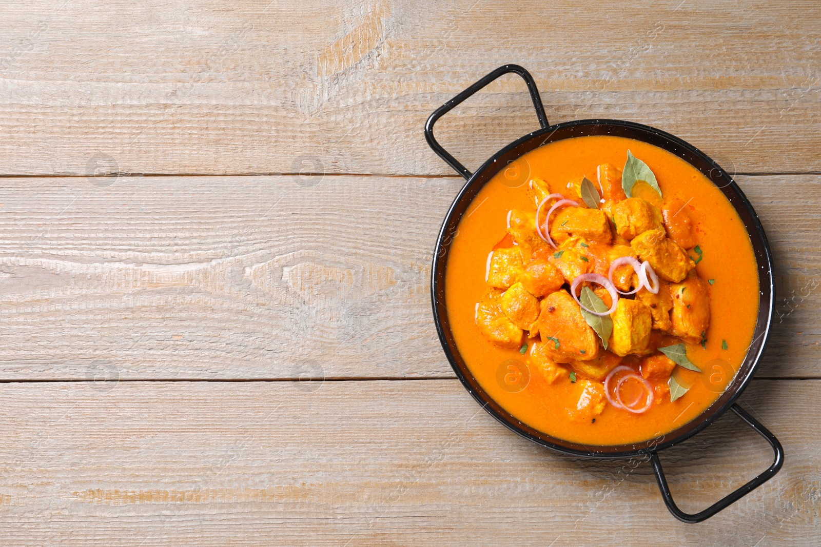 Photo of Delicious chicken curry in pan on wooden table, top view. Space for text