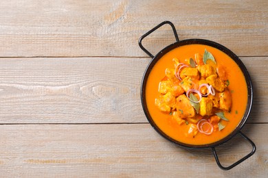 Photo of Delicious chicken curry in pan on wooden table, top view. Space for text