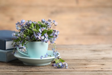 Beautiful forget-me-not flowers in cup and saucer on wooden table, closeup. Space for text