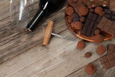 Photo of Bottle of red wine, glass, chocolate sweets and corkscrew on wooden table, above view. Space for text