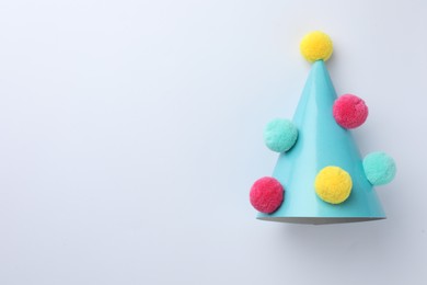 Photo of One blue party hat with pompoms on light background, top view. Space for text
