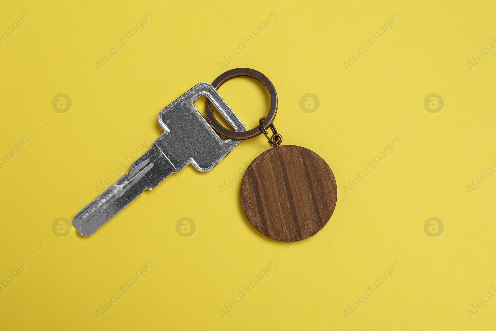Photo of Key with wooden keychain in shape of house on yellow background, top view