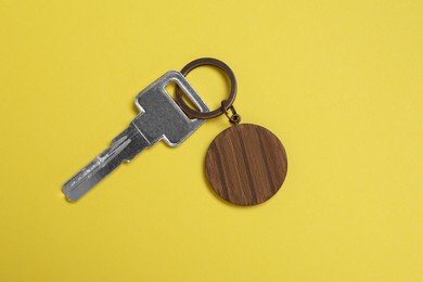 Key with wooden keychain in shape of house on yellow background, top view