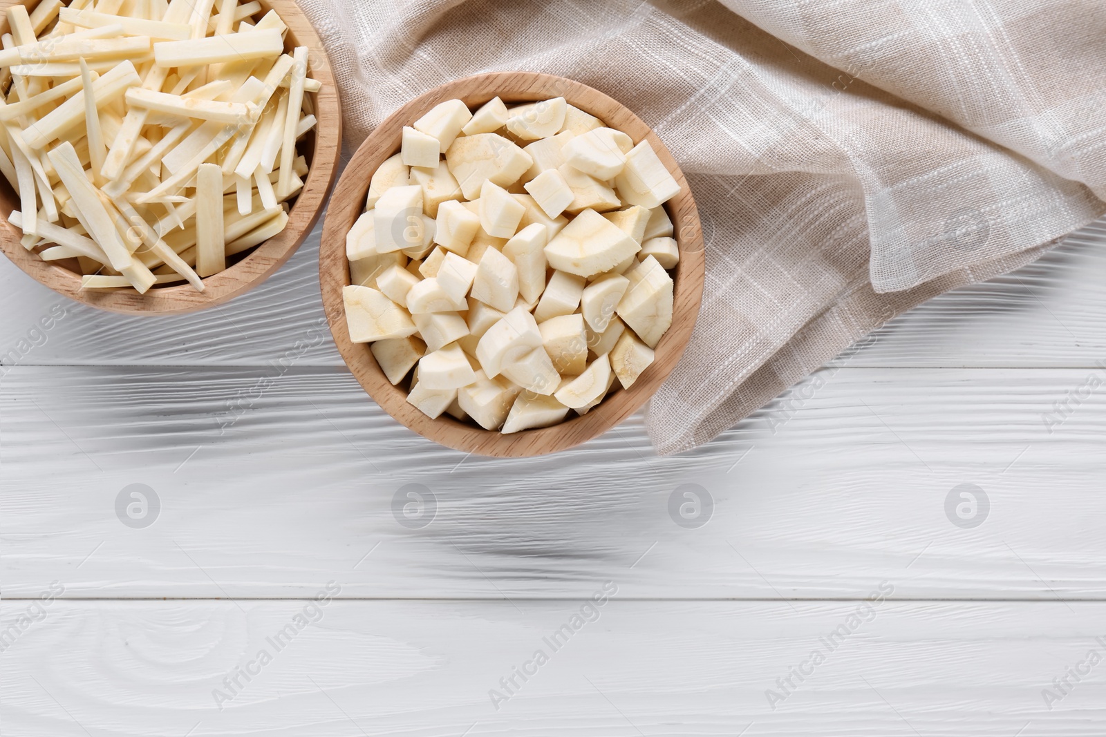 Photo of Bowls with cut parsnip on white wooden table, flat lay. Space for text