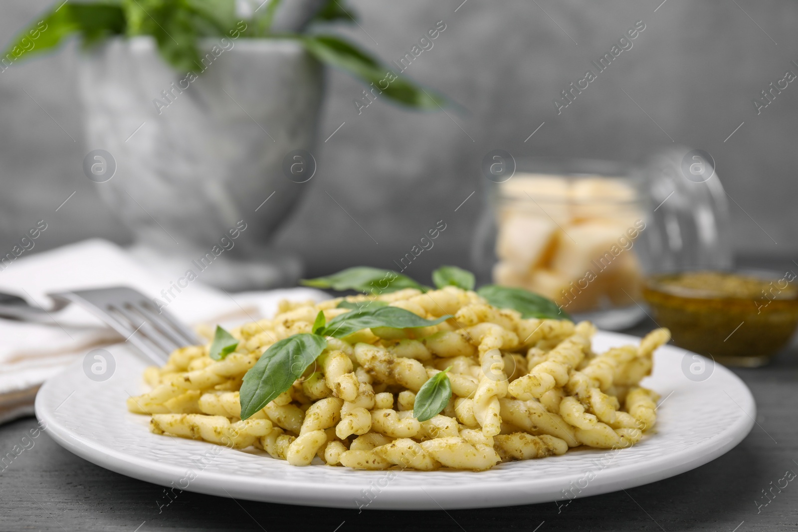 Photo of Plate of delicious trofie pasta with pesto sauce and basil leaves on grey wooden table