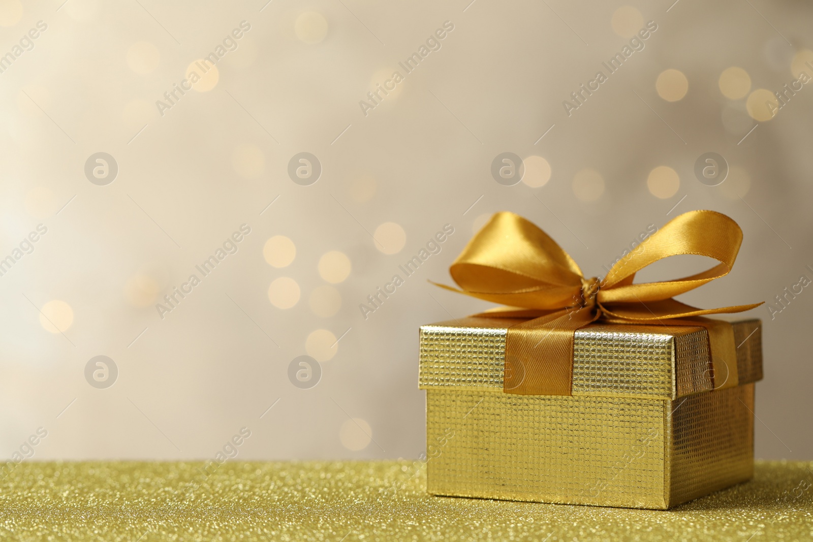 Photo of Beautiful gift box on golden table against blurred festive lights, space for text