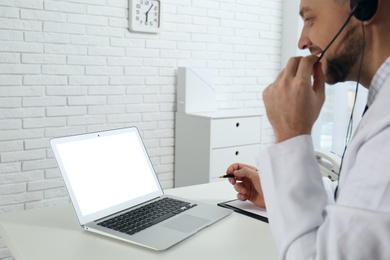 Photo of Doctor with headset consulting patient online at desk in clinic, space for text. Health service hotline