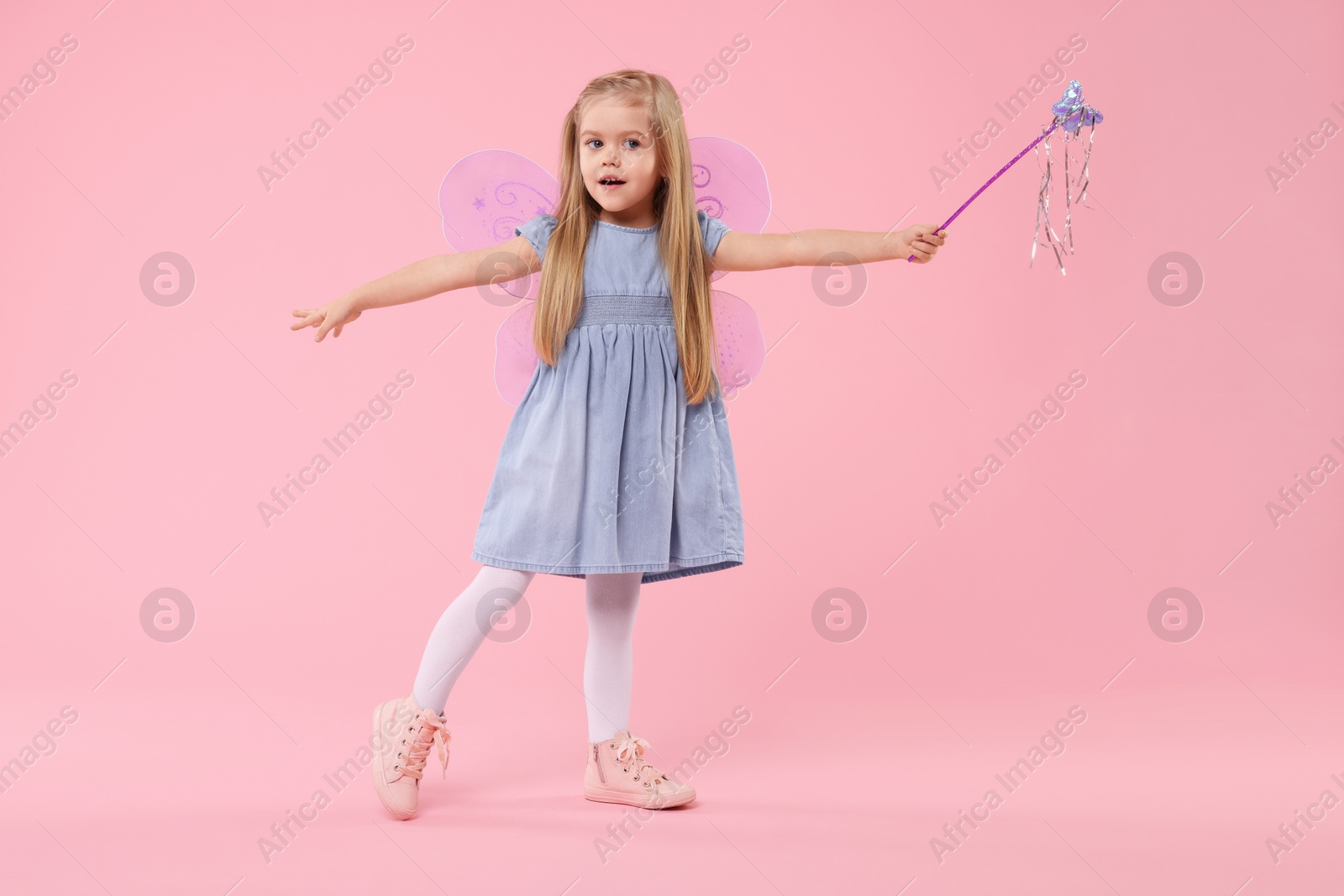 Photo of Cute little girl in fairy costume with violet wings and magic wand on pink background