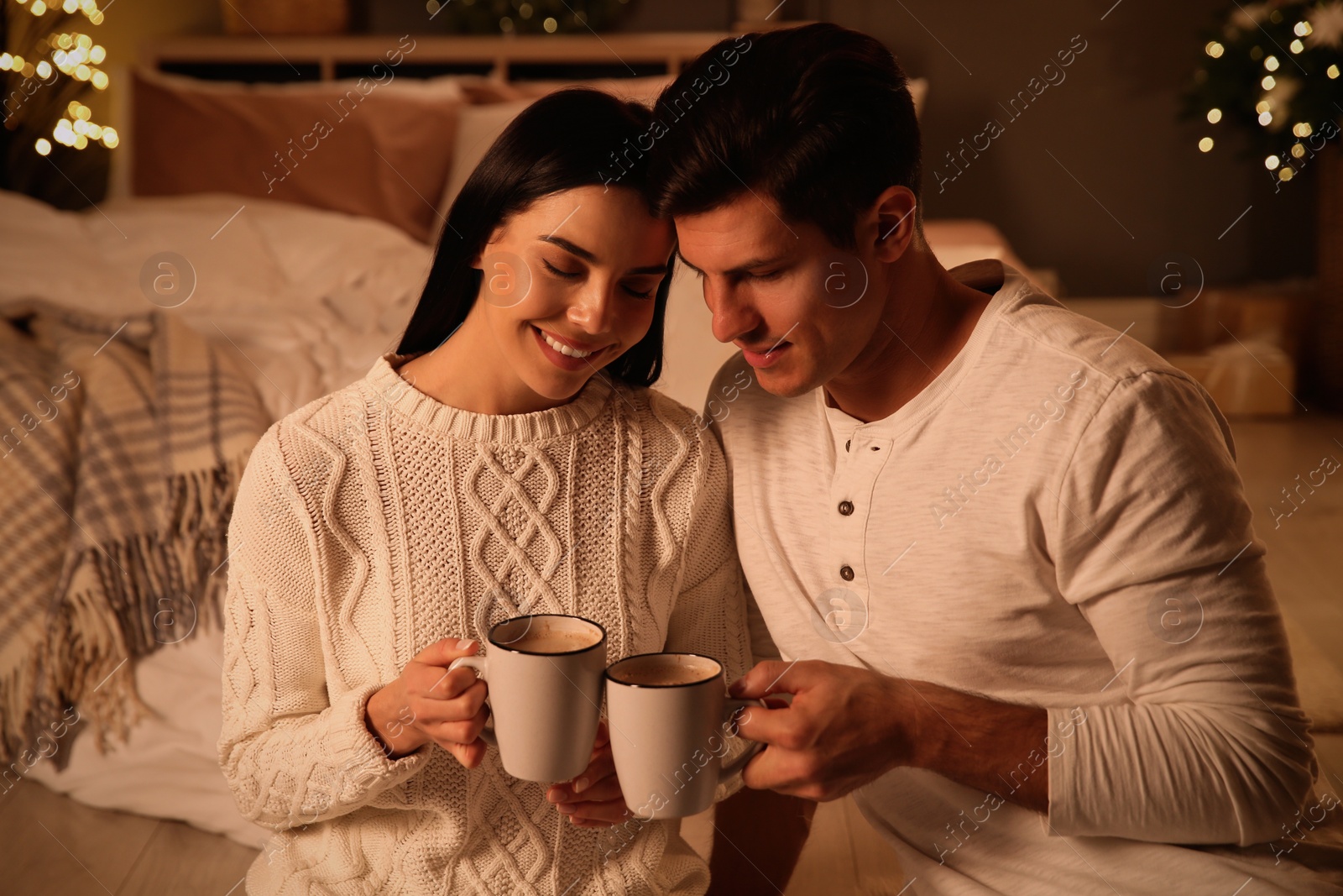 Photo of Happy couple with cups in festively decorated bedroom. Christmas celebration