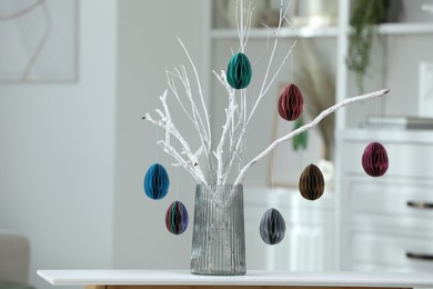 Branches with paper eggs in vase on white table indoors, space for text. Beautiful Easter decor