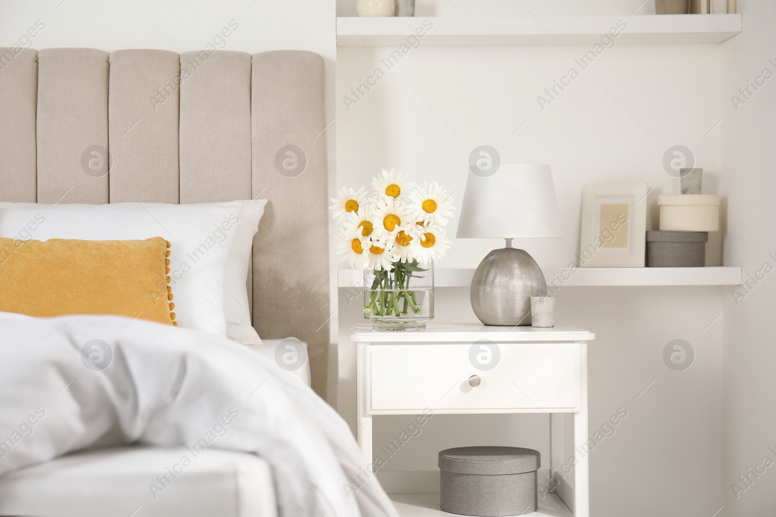 Photo of Bouquet of beautiful daisy flowers and lamp on nightstand in bedroom