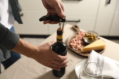 Man opening wine bottle with corkscrew at table indoors, closeup